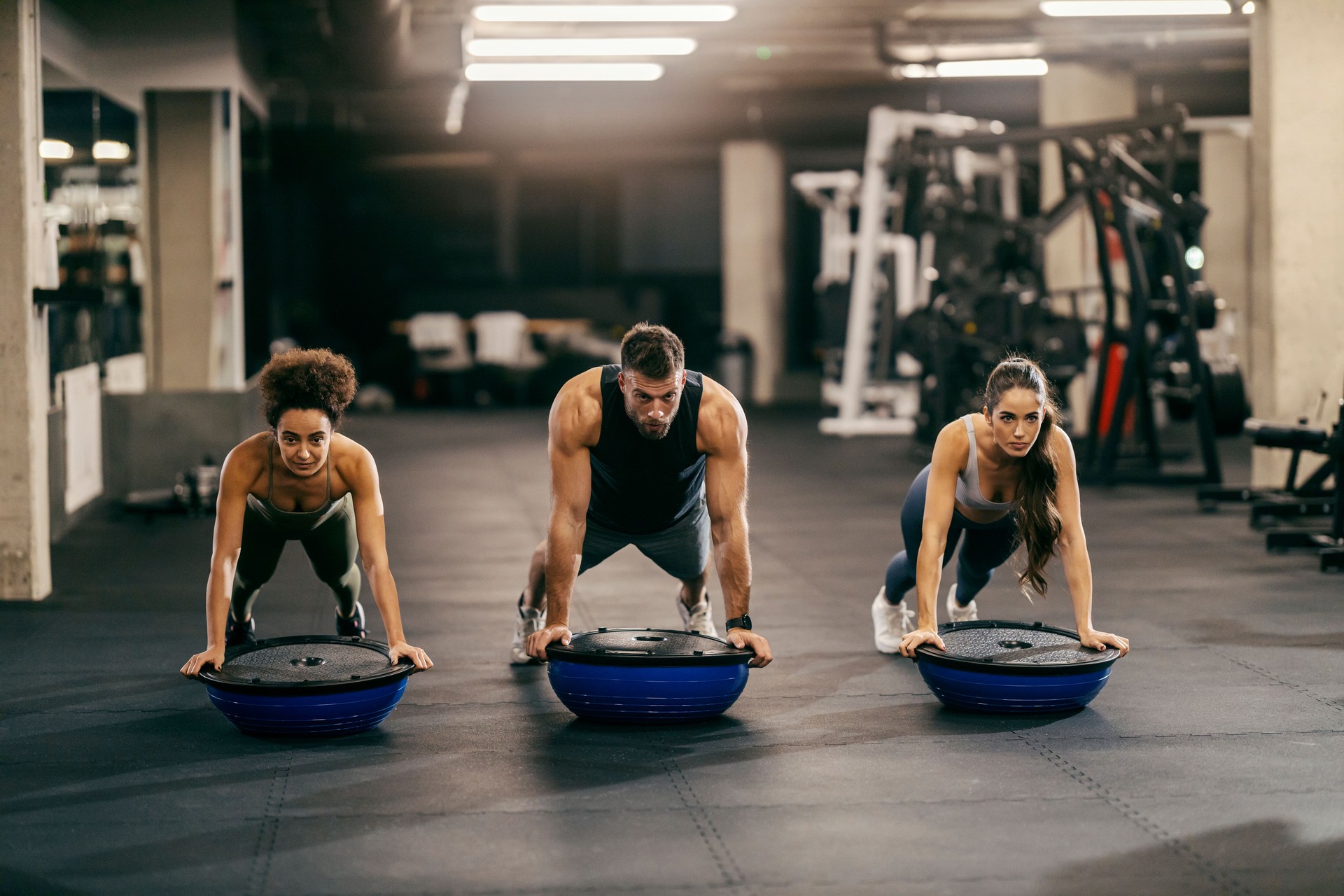 Fit muscular sportspeople doing planks endurance with bosu ball in a gym.