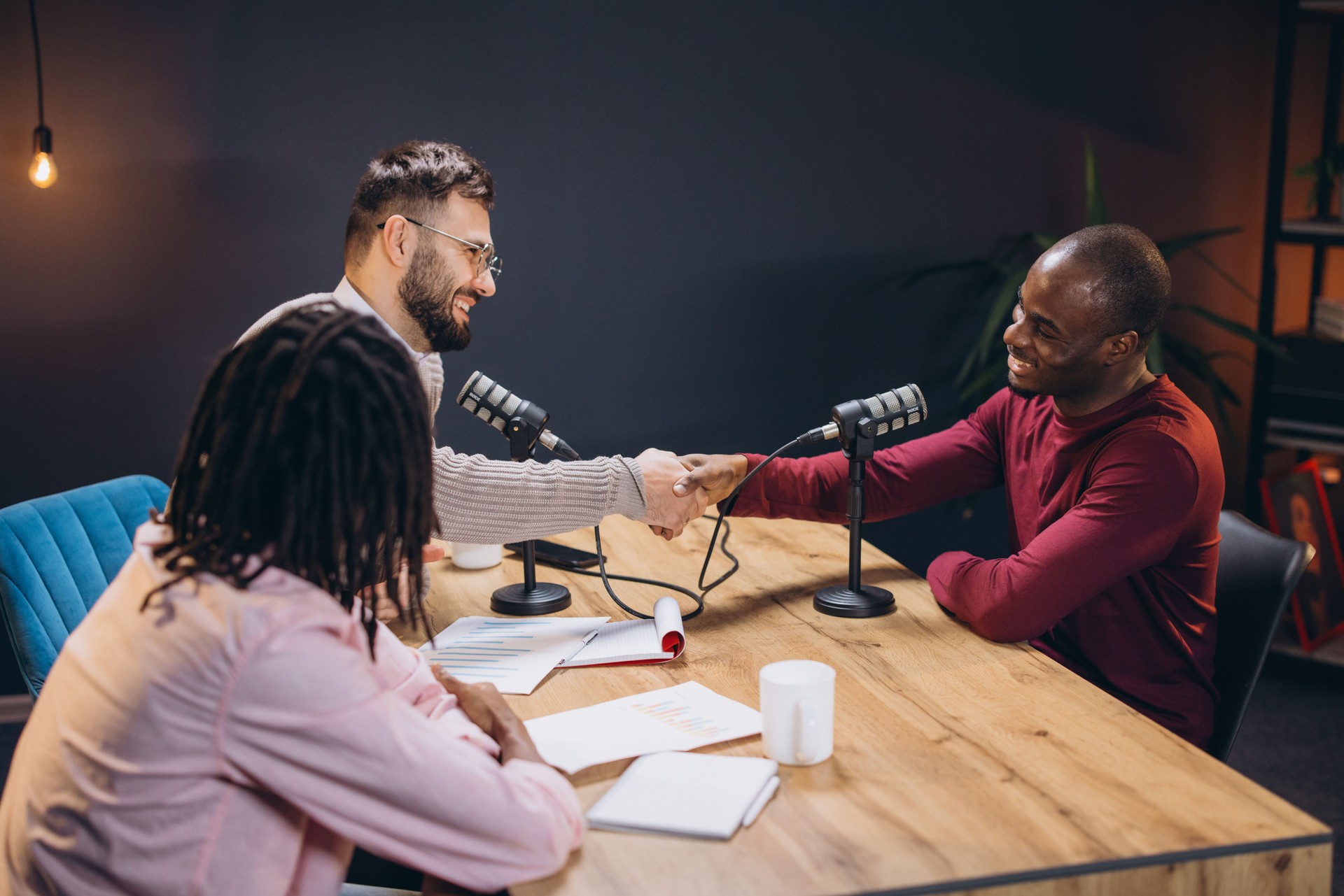 Radio hosts greeting guest while recording podcast in soundproof professional broadcasting studio